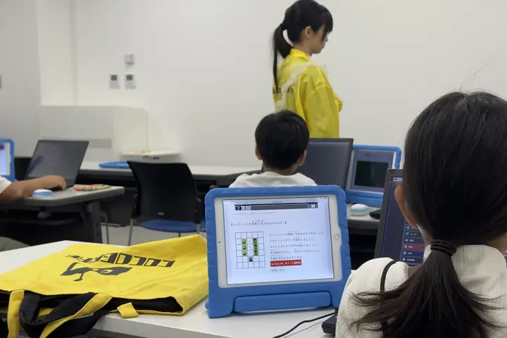 タブレットの教材を見ながら課題に取り組む子どもたちと、見守る講師